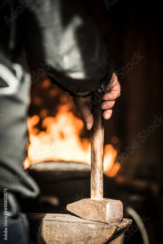Hammer in right hand resting on anvil, fire in black background