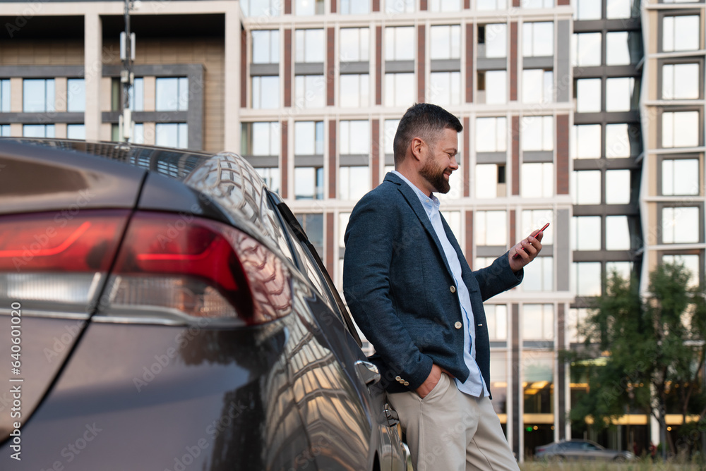 Businessman using smartphone near the car on the background of a skyscraper Businessman using smartphone near the car on the background of a skyscraper