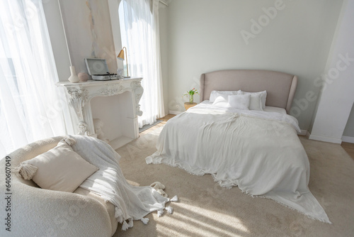 a gentle cozy bright apartment with huge panoramic windows with sunlight. bedroom in soft beige tones with a fireplace and a comfortable stylish upholstered armchair and bed