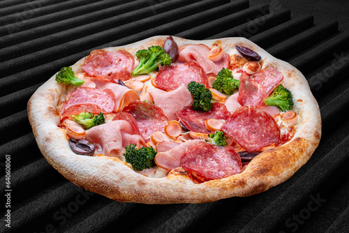 Pizza with salami, ham, vienna sausages, kalamata, olives, broccoli, pelati, pesto. Neapolitan round pizza on dark background