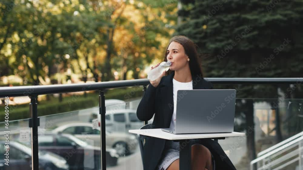 Young woman focusing on her work, looking at laptop screen, nomad remote workplace, sitting on rooftop outdoors with relaxing view with bottle of water. Young woman focusing on her work, looking at laptop screen, nomad remote workplace, sitting on rooftop outdoors with relaxing view with bottle of water.