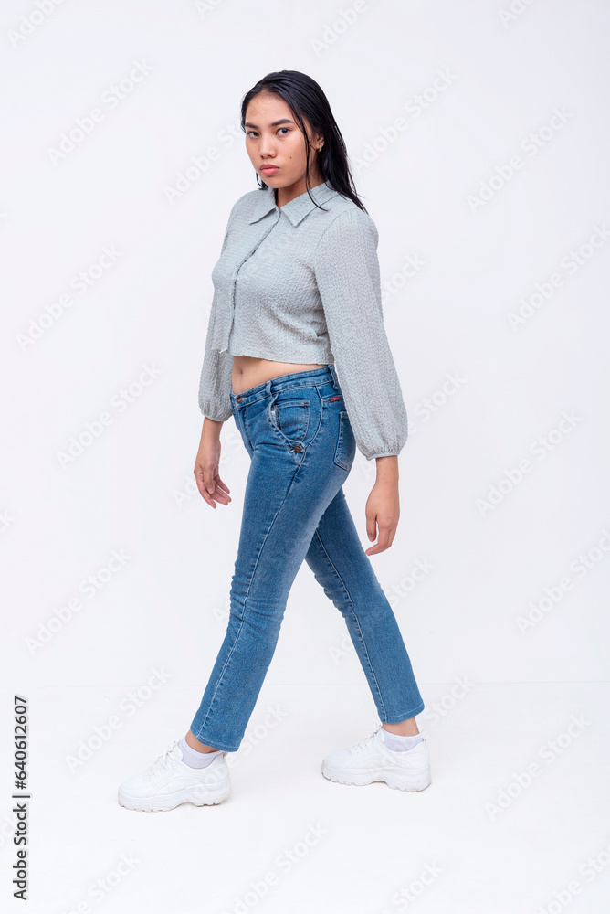 Side view of a asian woman with mid-length straight hair in a long sleeved cutoff blouse and blue jeans walking. Possible college student. Isolated on a white backdrop. Side view of a asian woman with mid-length straight hair in a long sleeved cutoff blouse and blue jeans walking. Possible college student. Isolated on a white backdrop.