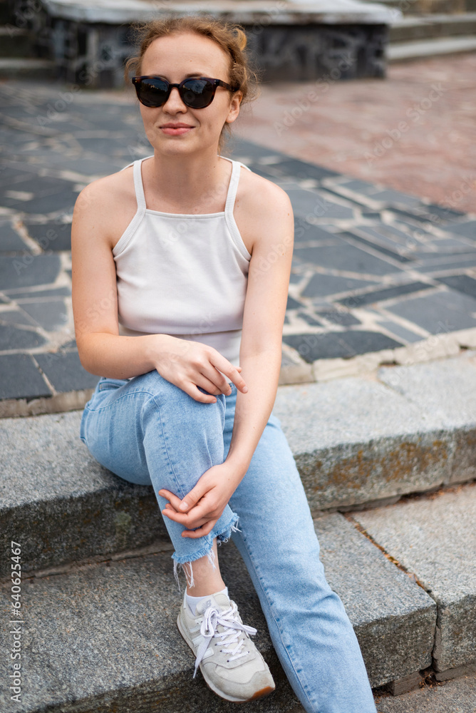 A woman wearing sunglasses is sitting on a staircase on the street A woman wearing sunglasses is sitting on a staircase on the street