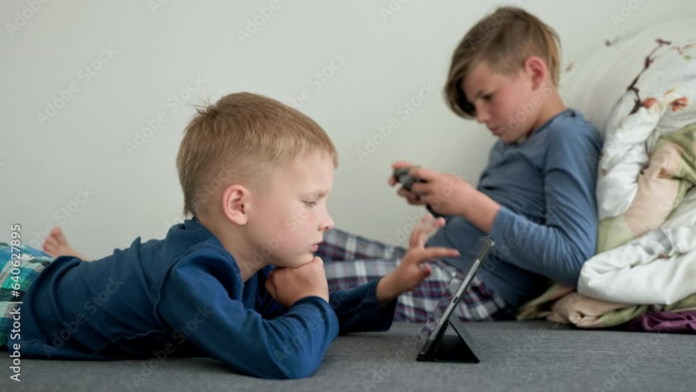 childrens dependence on gadgets, cute boys play electronic devices lying on sofa in room childrens dependence on gadgets, cute boys play electronic devices lying on sofa in room