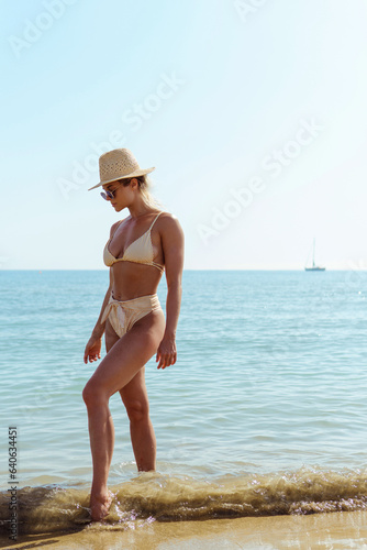 Woman radiates summer vibes wearing yellow striped bikini and a straw hat, enjoying her time on the sandy beach