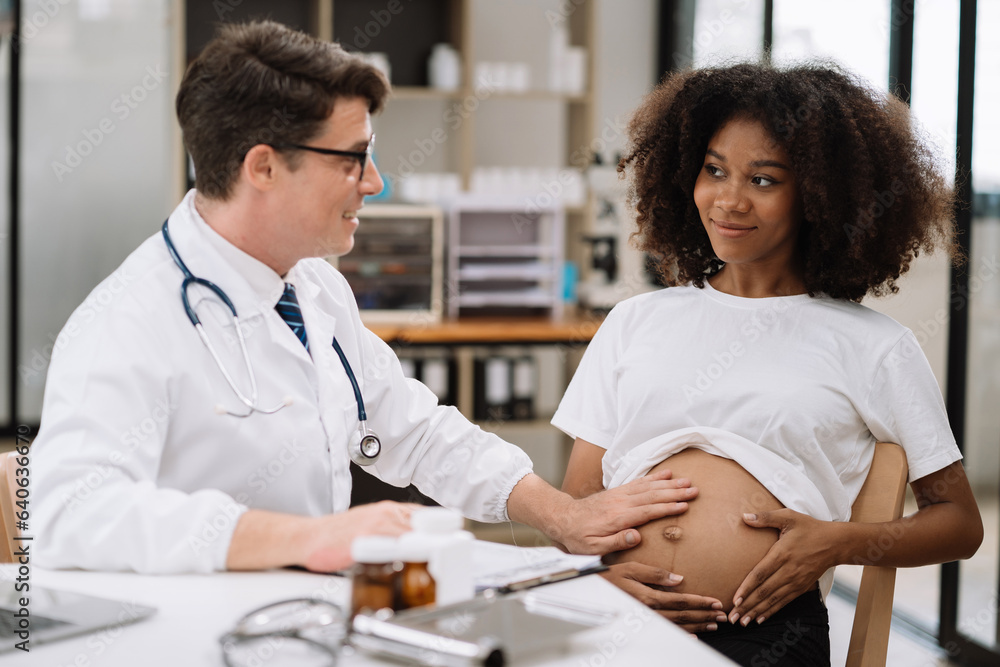 Happy pregnant woman has appointment with doctor at clinic. male  medic specialist with stethoscope listens to baby's heartbeat in mother's belly. Pregnancy, health care concept.