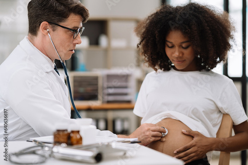 Happy pregnant woman has appointment with doctor at clinic. male  medic specialist with stethoscope listens to baby's heartbeat in mother's belly. Pregnancy, health care concept. photo