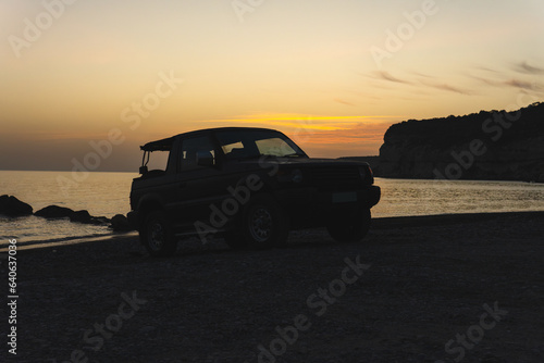 Sunset silhouette of a convertible SUV on a pebble beach