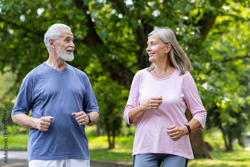 Senior couple of pensioners jogging in the park, gray-haired man and woman joyfully running, active lifestyle.