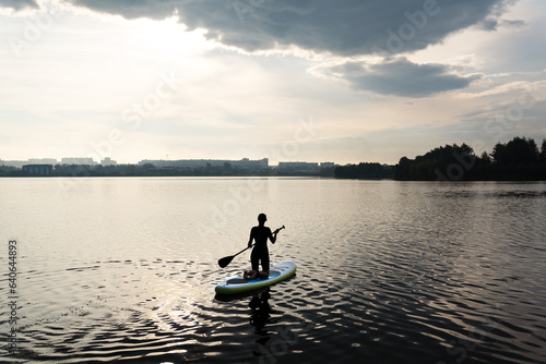 Water sports  surf lessons  the appearance of a girl against the backdrop of a sunrise. Stand on a kayak on the water with the warm colors of a summer sunset.