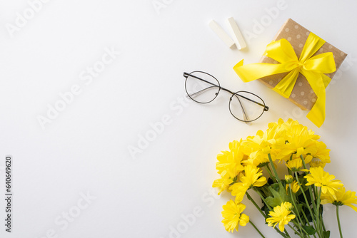 Celebrate Teacher\'s Day uniquely. A top-view picture showcases chalk, glasses, bunch of chrysanthemums and a gift box on a white isolated backdrop. Ample space for text or promotional content