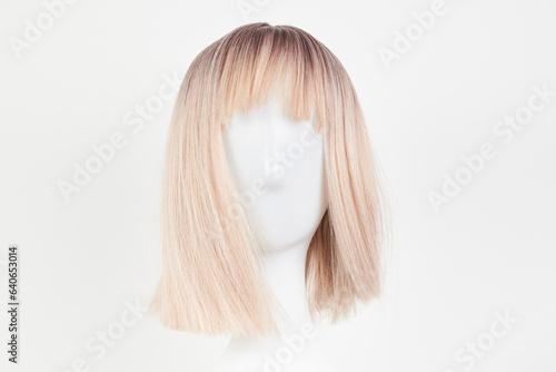 Natural looking blonde fair wig on white mannequin head. Short hair cut on the plastic wig holder isolated on white background, front view.