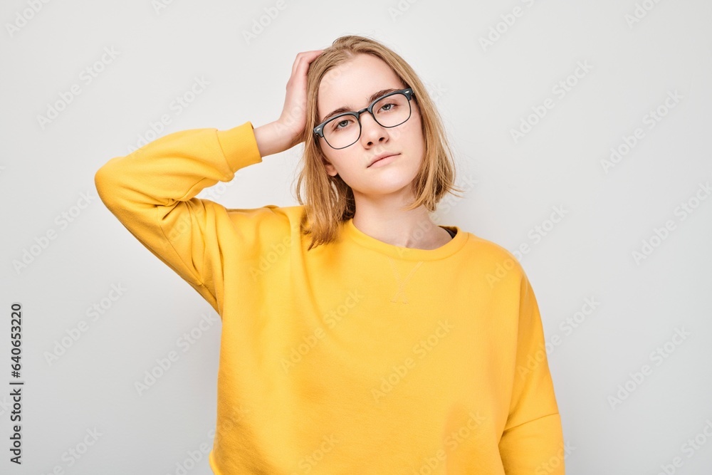 Clever blond student girl with glasses touches head thinks, chooses isolated on white studio background with copy space. Confidence smart genius Clever blond student girl with glasses touches head thinks, chooses isolated on white studio background with copy space. Confidence smart genius