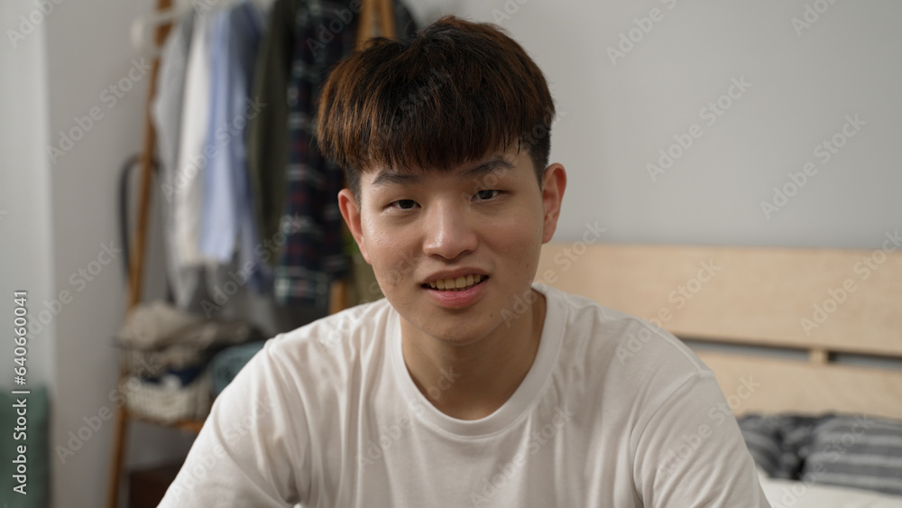 headshot of an embarrassed asian boy wearing t shirt is looking at the camera and scratching his head in modern bright bedroom at home headshot of an embarrassed asian boy wearing t shirt is looking at the camera and scratching his head in modern bright bedroom at home