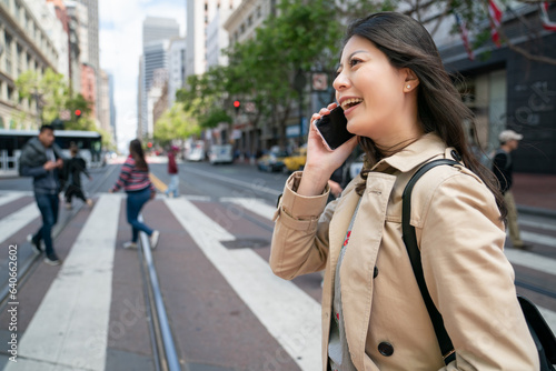 closeup of smiling asian Taiwanese business lady talking cheerfully on the phone while walking across street on zebra crossing in financial district of san Francisco in California usa