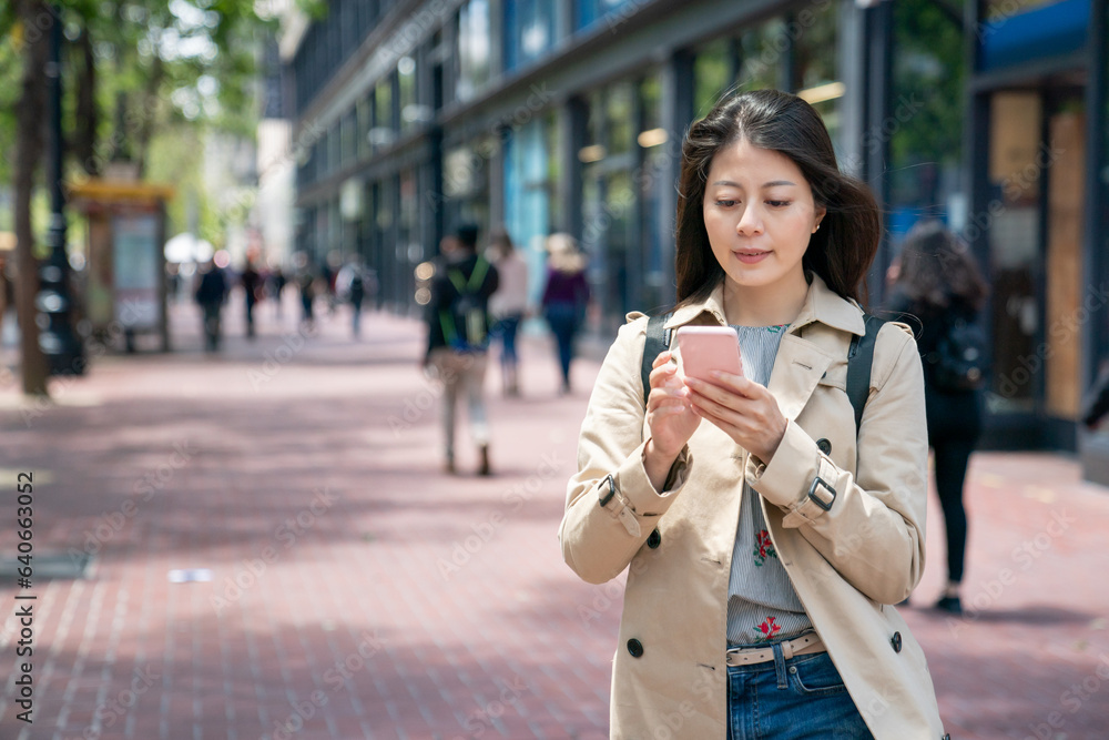 Fototapeta premium asian Japanese female traveler searching for travel information on the phone in the breeze while walking on the sidewalk in the financial district of san Francisco in California usa
