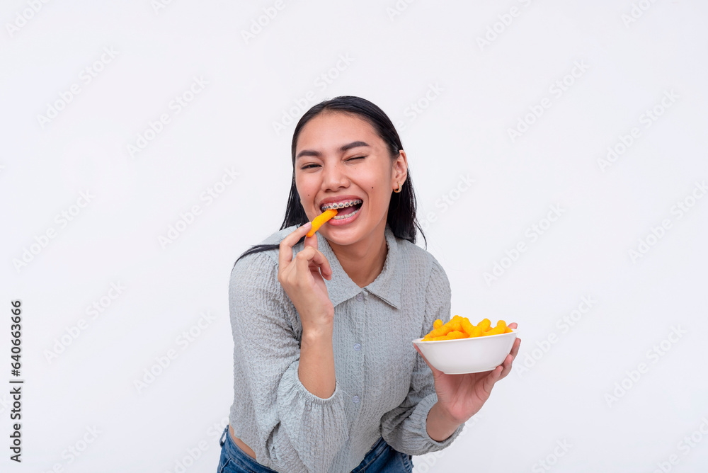 A cheerful young asian woman enjoying a bowl of cheese puffs. Having a delicious snack. Isolated on a white background.
