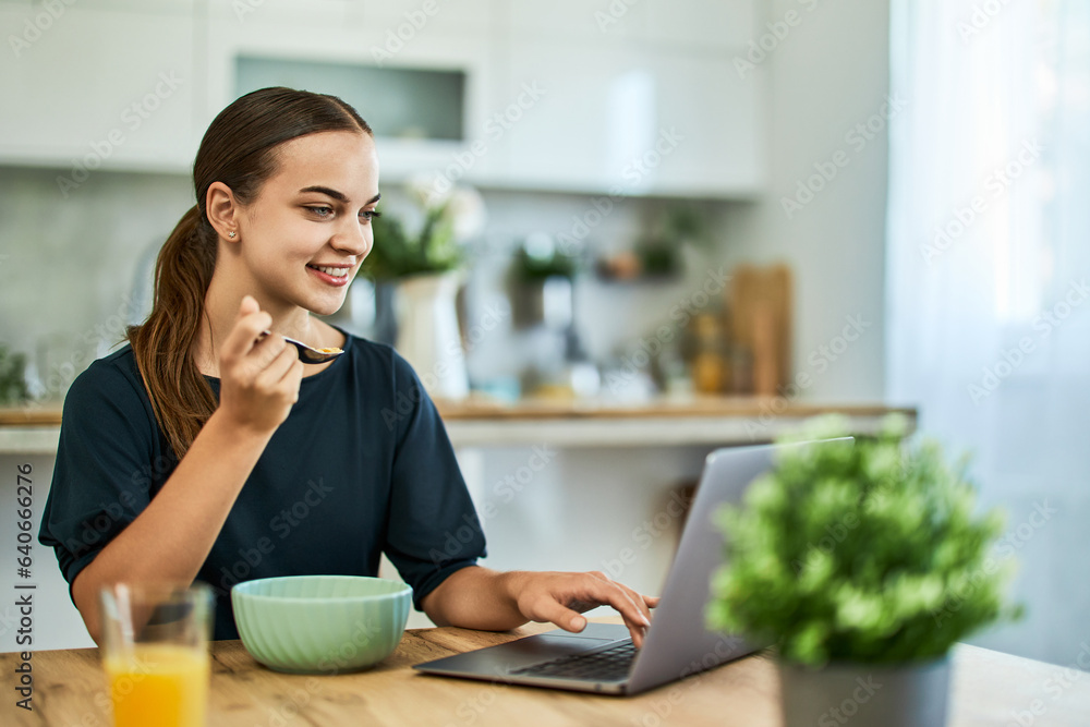 A smiling female freelancer eating cereal for breakfast while working on a laptop. A smiling female freelancer eating cereal for breakfast while working on a laptop.