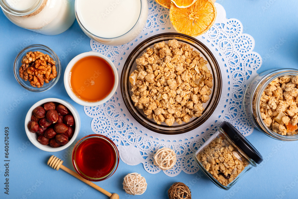 Tasty crispy granola, milk, honey, walnuts and hazelnuts from above on light blue background. Granola with milk for breakfast. Tasty crispy granola, milk, honey, walnuts and hazelnuts from above on light blue background. Granola with milk for breakfast.