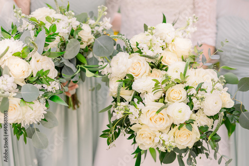 A bride and her bridesmaids hold a bouquet of classic white flowers and green leaves 