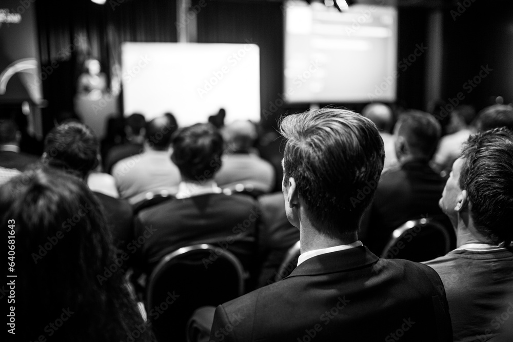 Fototapeta premium Speaker giving a talk in conference hall at business event. Rear view of unrecognizable people in audience at the conference hall. Business and entrepreneurship concept