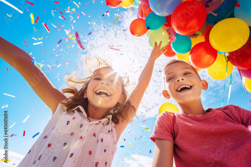 Fototapeta Cheerful funny child holding colourful balloons on a sky background. Kid having fun with balloons and confetti.