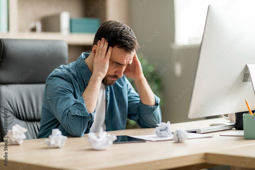 Inspiration Crisis. Pensive businessman sitting at workplace with crumpled paper on desk Inspiration Crisis. Pensive businessman sitting at workplace with crumpled paper on desk