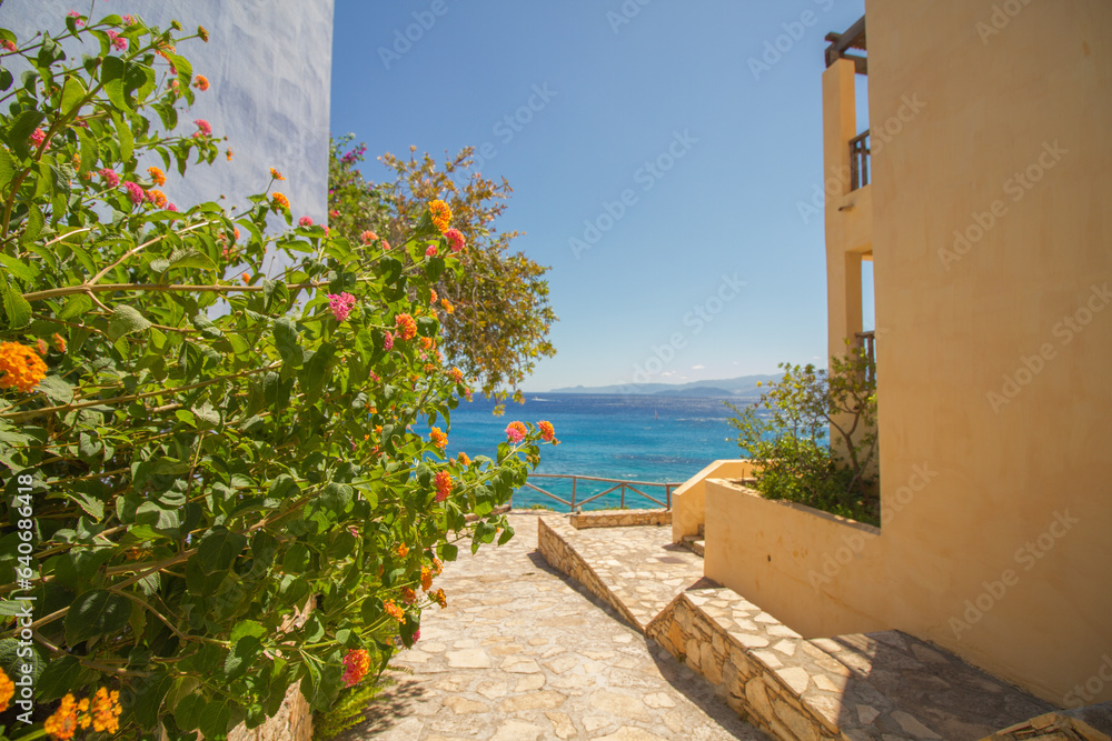 View of the turquoise mediterranean sea at the island of Crete, Greece, with traditional buildings and Lantana ‘Fruity Pebbles’ multicolor flowers, near Agios Nikolaos View of the turquoise mediterranean sea at the island of Crete, Greece, with traditional buildings and Lantana ‘Fruity Pebbles’ multicolor flowers, near Agios Nikolaos