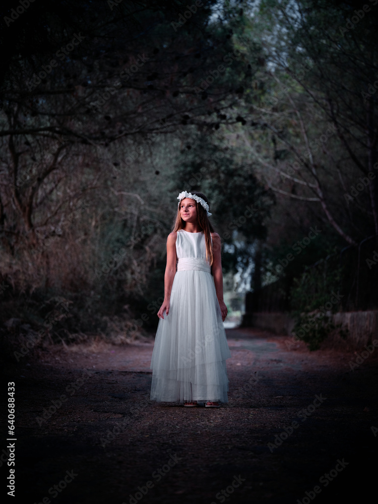 Elegant girl in white dress standing on dark path with closed gr Elegant girl in white dress standing on dark path with closed gr