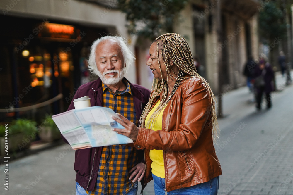 Multiracial senior couple having fun together during city trip looking on map - Focus on african woman face