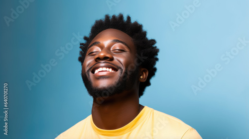Young man laughs against a blue background.