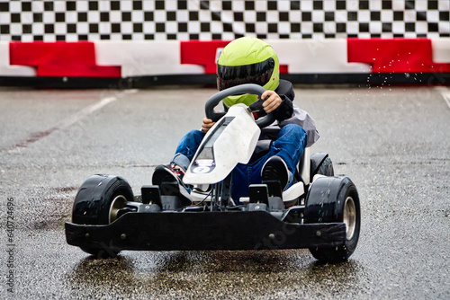 Young lover of extreme racing sports trains before a karting competition on the race track. Brave boy child racer in helmet driving children's electric karting
