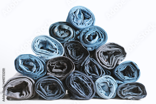 Pyramid of rolled up denim jeans on a white background. Trendy denim clothing, shopping, fashion, consumption.