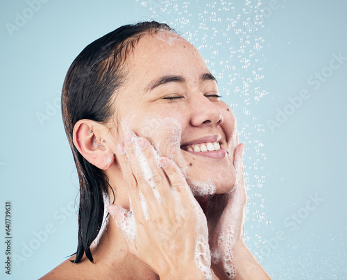 Skincare  shower soap and happy woman cleaning in studio isolated on a blue background. Water splash  hygiene foam and model smile  washing and bathing in wellness  healthy skin or beauty in bathroom
