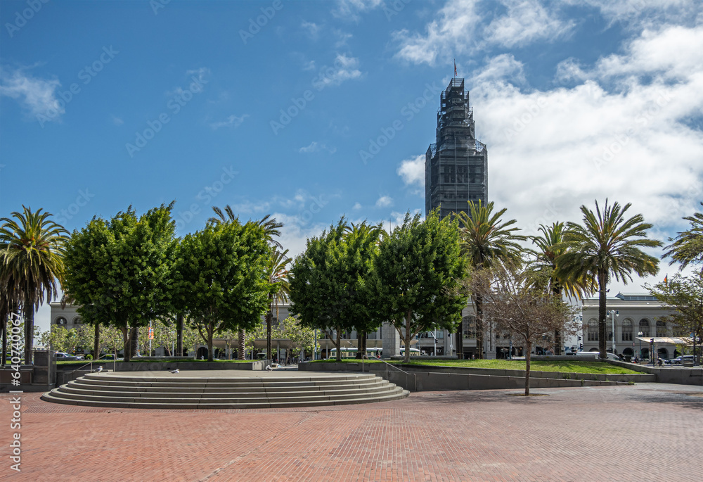 San Francisco, CA, USA - July 12, 2023: embarcadero plaza with green section in front of Ferry building clock tower in scaffolds under blue cloudsccape