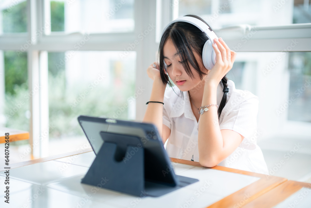 Happy of cute smiles Asian of attractive young Cute girl little wearing headphones and listening music using laptop computer working from at the cafe.Online education, elearning concept. Happy of cute smiles Asian of attractive young Cute girl little wearing headphones and listening music using laptop computer working from at the cafe.Online education, elearning concept.