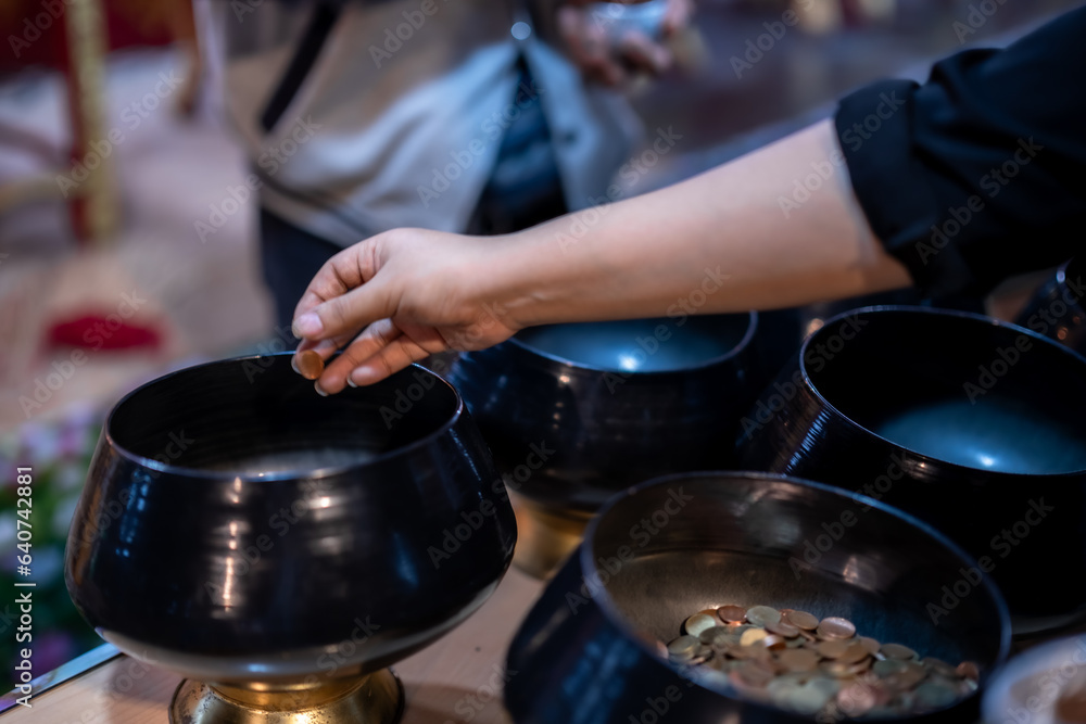 close up hand Asian woman tourist Make merit by dropping coins into the alms bowl. to Buddha for worship with faith to Buddha statue in temple thailand belief in Buddhism