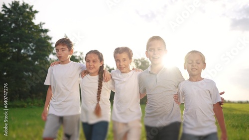 a group of children walk on the grass in the park hugging each other. happy family childhood dream concept. little kids are smiling and walking across the lifestyle field on the grass at sunset © maxximmm