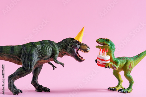 Cute happy green dinosaurs in birthday hats holding cake with flaming candles on pastel pink background. Copy space. Minimal art birthday card idea.