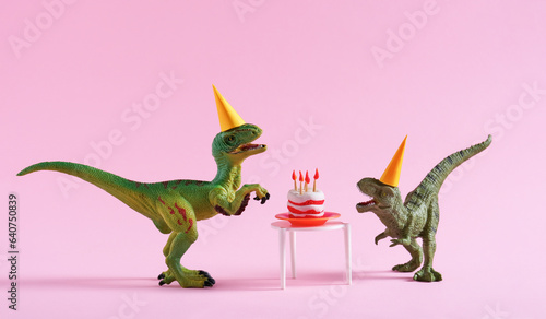 Cute happy green dinosaurs in birthday hats with cake with flaming candles on pastel pink background. Copy space. Minimal art birthday card idea.
