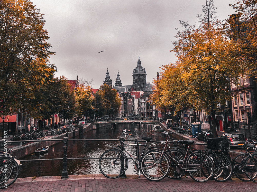 Fototapeta premium Amsterdam Bicycles. A tree lined canal in Amsterdam showcases the leaves turning yellow. In the foreground is a bridge with bicycles resting against the railing.