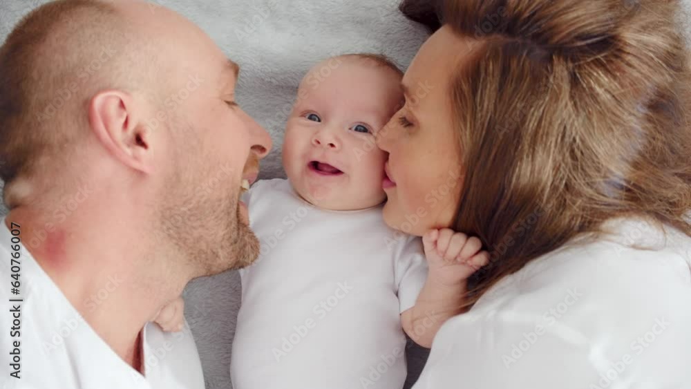 Close up Faces of the mother, father and infant baby. .Newborn baby with happy parents, top view. Happy family. Healthy newborn baby in a white t-shirt with mom and dad. Cute Infant boy and parents Close up Faces of the mother, father and infant baby. .Newborn baby with happy parents, top view. Happy family. Healthy newborn baby in a white t-shirt with mom and dad. Cute Infant boy and parents
