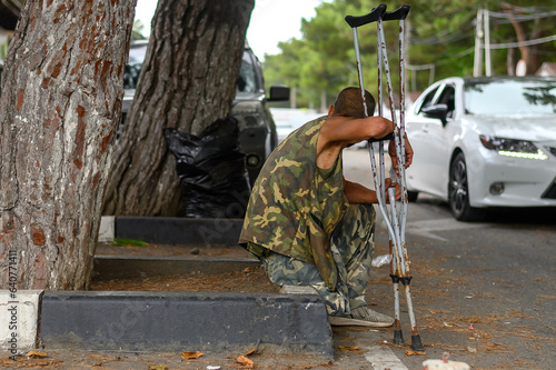 A disabled beggar with crutches begging on the street in summer. photo