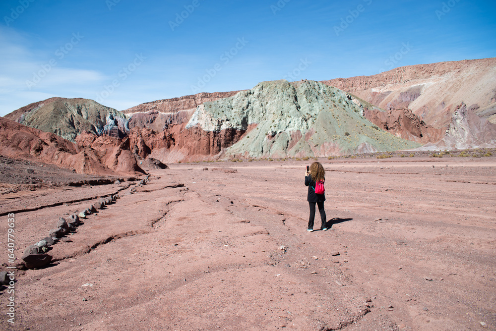 woman with red backpack taking a picture at the green rocks of valle arcoiris, antofagasta, atacama, chile