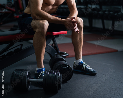 Faceless shirtless man sitting on a bench and resting after a workout. 