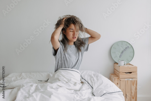 Asian woman just wake up by the clock at 7 AM on the bed in the morning. photo