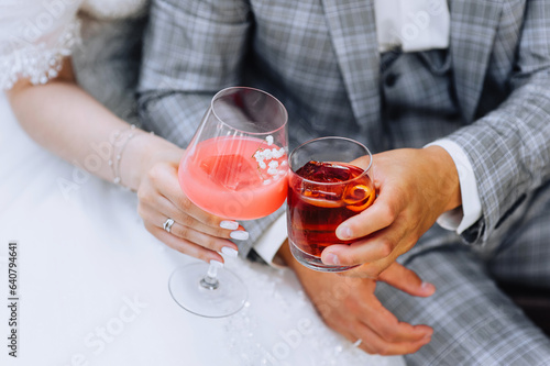 The bride and groom are holding glass glasses with an alcoholic cocktail, whiskey with ice in their hands at a bar party. Wedding photography, close-up portrait.