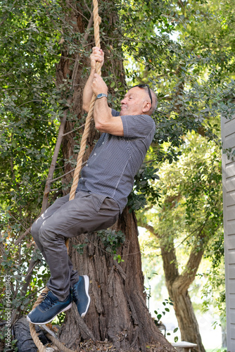 Active Aging Triumph. 75-Year-Old Man Backyard Rope Climb, Shattering Age Stereotypes with Vibrant Sports Engagement.