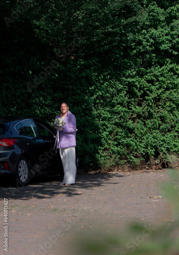 Modern bride with wedding flowers and wearing purple jacket getting out of a car