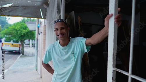 One happy black Brazilian young man standing by sidewalk street smiling at camera. Authentic real life from South America portrait with friendly expression